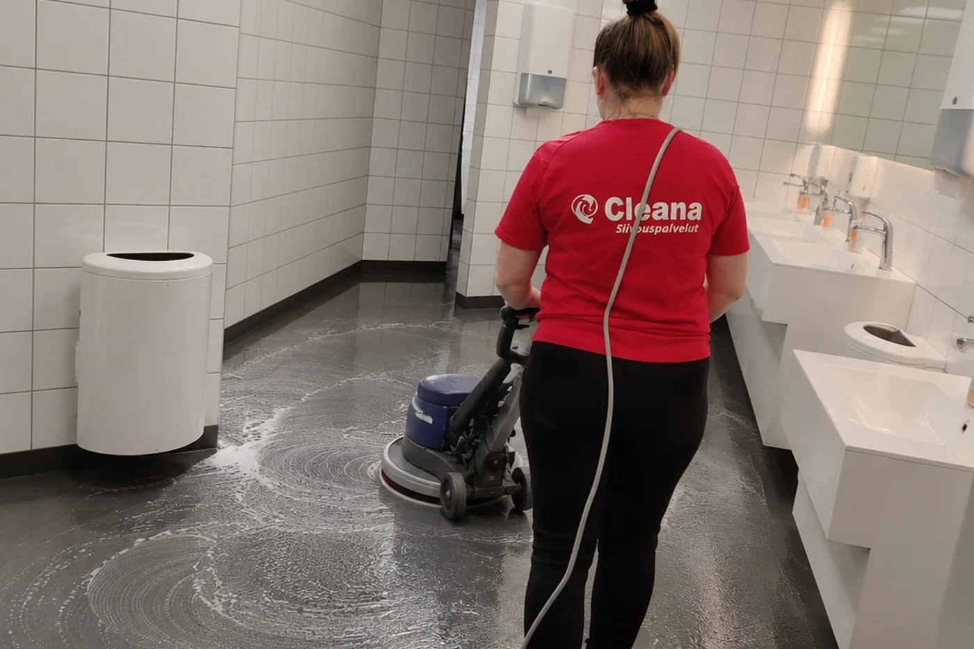 Cleanan ty&ouml;ntekij&auml; pesee WC-tilan lattiaa yksilaikkakoneella
